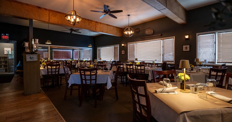 Interior with tables set with white tablecloths and yellow flowers, under warm lighting