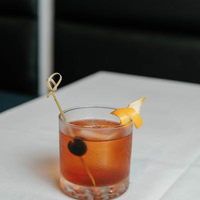 A glass of Old Fashioned garnished with lemon peel and cherry.