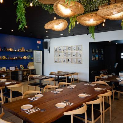 Dining area, wooden tables and chairs, featuring hanging rattan light fixtures and greenery.