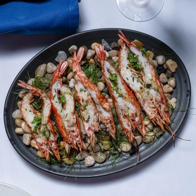 Grilled prawns served over pebbles with herbs on a black plate.