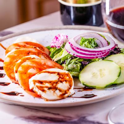 Caprese salad with tomatoes, mozzarella, and a side salad, paired with red wine.