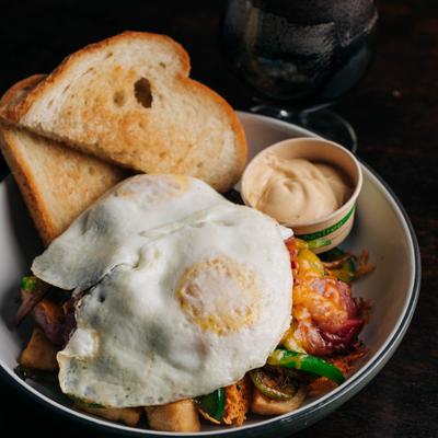 Breakfast hash topped with eggs and served with toast and creamy sauce.