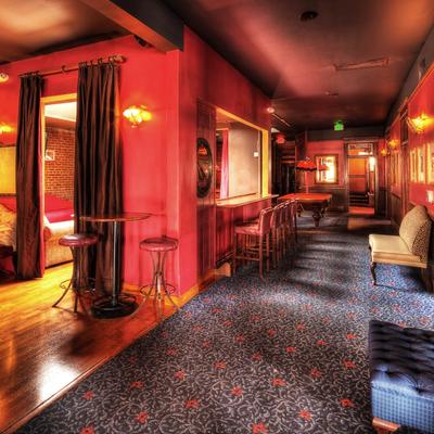 Lounge with dim lighting, featuring red walls, a patterned carpet, bar stools, and a pool table