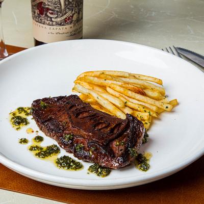 Skirt steak topped with chimichurri, served with fries on a white plate.