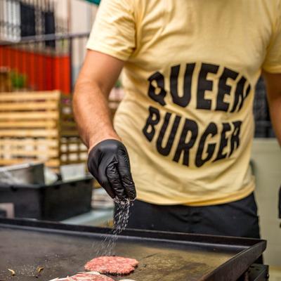 Restaurant employee grilling burgers, wearing a yellow Queen Burger T-shirt