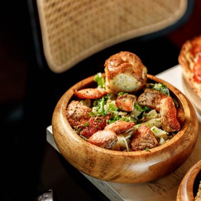 A wooden bowl filled with pasta, grilled salmon, broccoli, and fresh herbs.