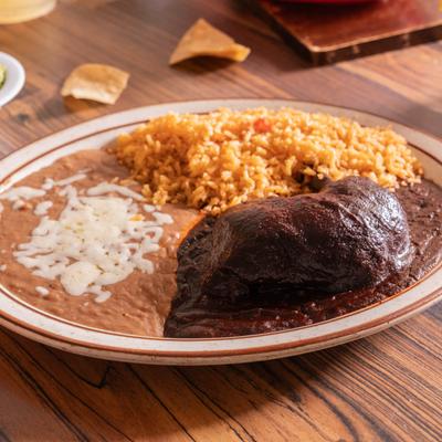 Chicken leg in mole sauce, served with rice, and refried beans.