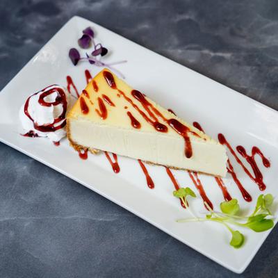 A slice of cheesecake drizzled with berry sauce.