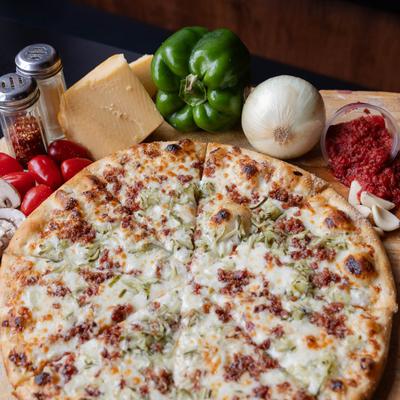 Pickle pizza surrounded by fresh ingredients like tomatoes, herbs, onions, and cheese blocks.