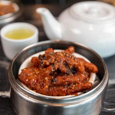 Spicy chicken feet served in a dim sum steamer, alongside a teapot and a cup of tea.