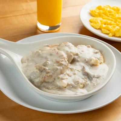 Biscuits and gravy serrved alongside scrambled eggs and a glass of orange juice.