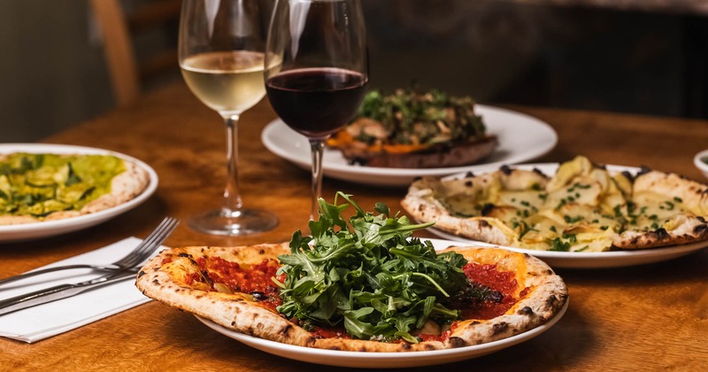 Assortment of pizzas on a wooden table, with two glasses of red and white wine