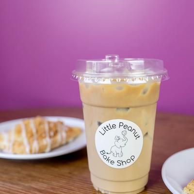 Iced coffee in a clear cup with the  Little Peanut Bake Shop logo.