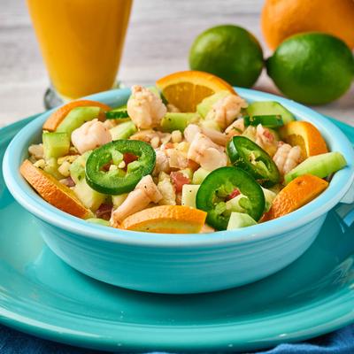 Ceviche topped with jalapenos, surrounded by limes and a drink.