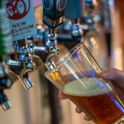 A hand holds a tilted glass, filling it with amber beer from a tap.