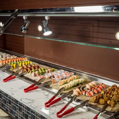 A long buffet counter is filled with various colorful rolls of sushi.