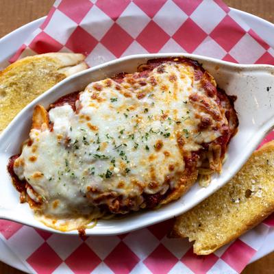 Chicken Parmesan with spaghetti served in a white casserole dish with garlic bread.