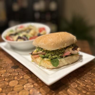 Chicken pesto sandwich served on a toasted ciabatta roll with a small side salad.