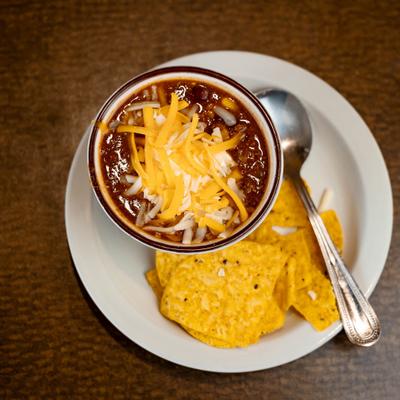 Bowl of chili topped with cheese, served with chips on the side.