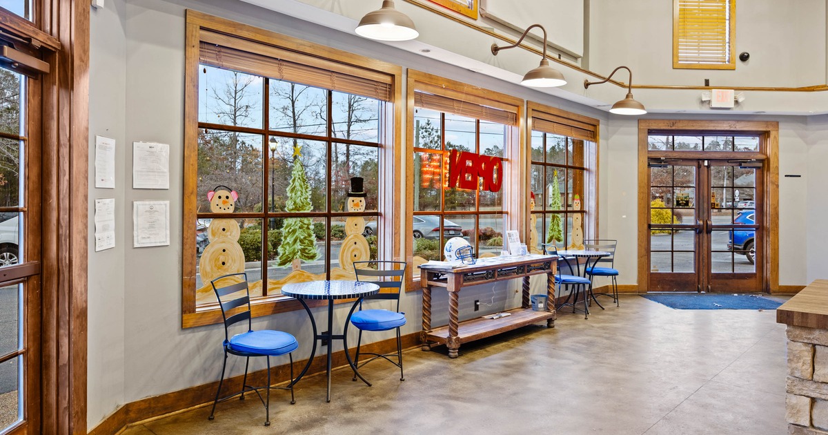 Interior with large windows featuring holiday paintings, blue chairs, tables, and an 
