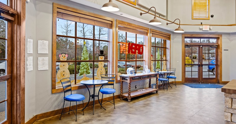 Interior with large windows featuring holiday paintings, blue chairs, tables, and an "OPEN" sign