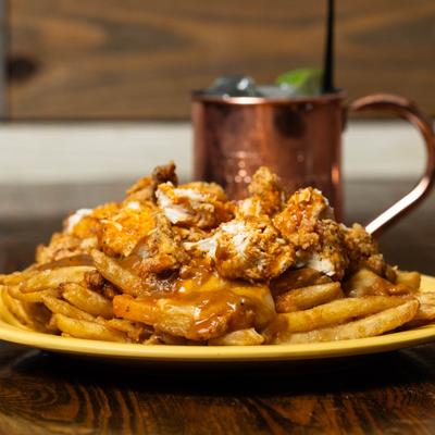 Buffalo Poutine topped with chicken, alongside a cocktail in a coper mug.