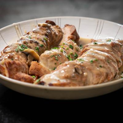 Rolled chicken in creamy sauce on a round plate.