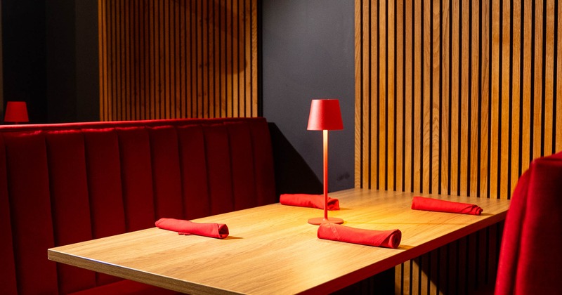 Restaurant booth with red seating, wooden table, red lamp and pendant lighting