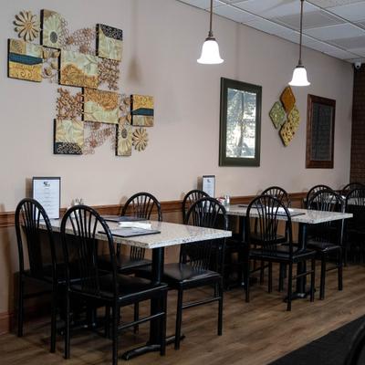 Dining room, tables with stone patterned tops, black chairs, wooden flooring, wall decorations.