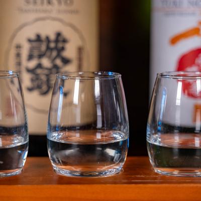 Three sake tasting glasses filled with clear sake on a wooden board.
