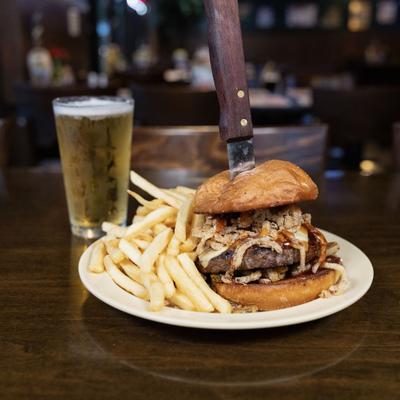 Angus Burger topped with fried onion strips, served with fries and a glass of beer.
