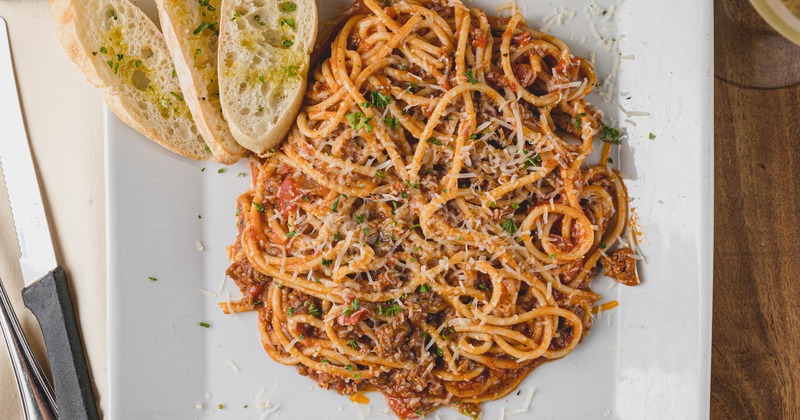 Spaghetti Bolognese served on a square white plate with garlic bread