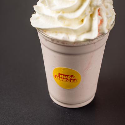 Milkshake in a branded plastic cup, topped with whipped cream and a cherry.