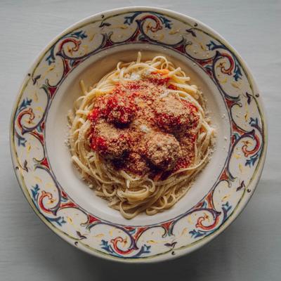 A colorful, ornate plate holds spaghetti with red sauce and meatballs, sprinkled with grated cheese.