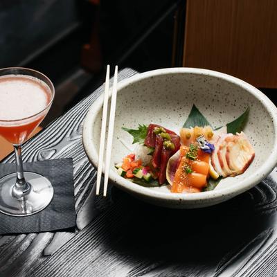 Elegant sashimi bowl with assorted fish alongside a cocktail.