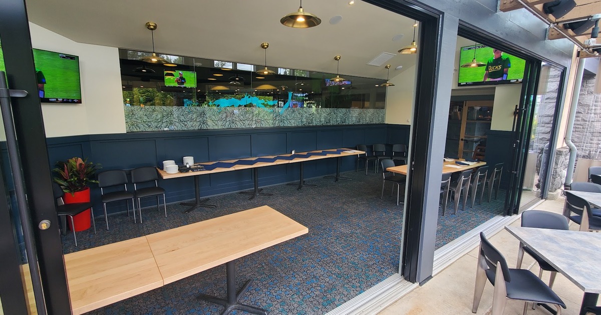 Interior with two long wooden tables, and TVs showing sports