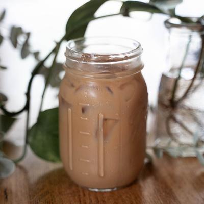 An iced coffee on a wooden table with plants in the background.