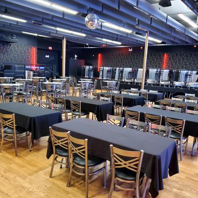 Banquet hall set up with long rectangular tables covered in dark tablecloths.