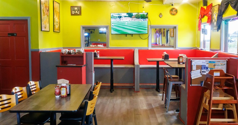 Interior of a vibrant restaurant with green walls, red booths, and a wall-mounted TV