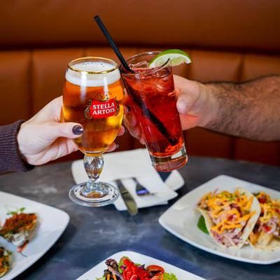 Hands clinking beer and cocktail glasses over a restaurant table.