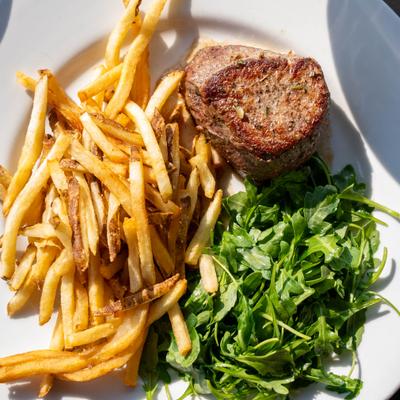 Filet mignon served alongside fries and arugula salad on a white plate.