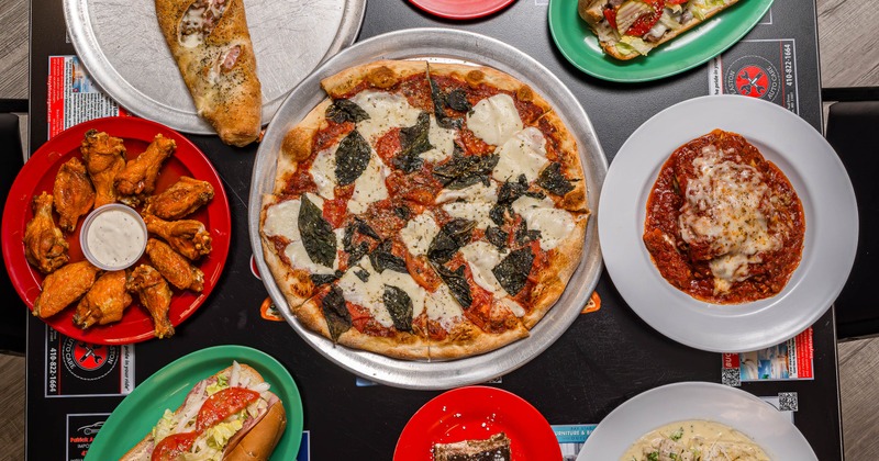 Spread of assorted dishes including pizza, wings, and sandwiches
