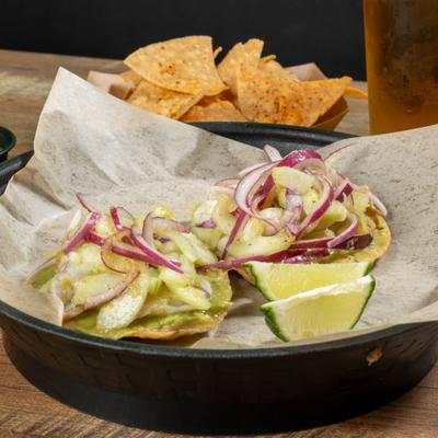 Two shrimp tostadas served with tortilla chips and lime wedges.