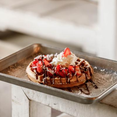 Waffle topped with strawberries, chocolate drizzle and whipped cream.
