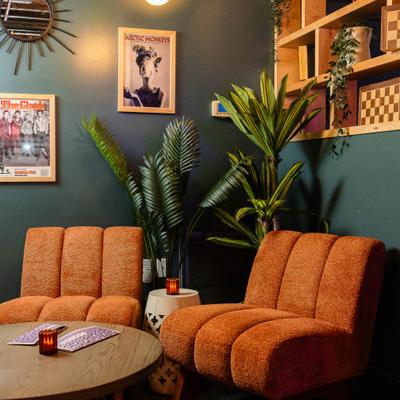 Lounge area featuring orange, tufted chairs, potted plants and a dark green wall.