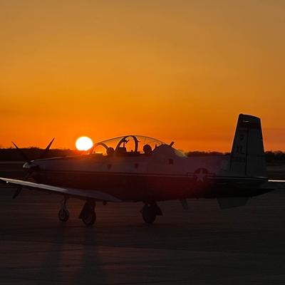 A small plane parked on a runway during a beautiful sunset.