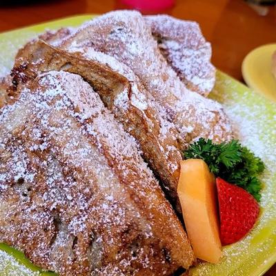 French toast, dusted with powdered sugar and served with slices of fruit.