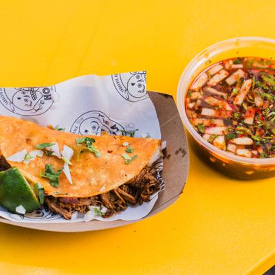 Birria Taco served in a paper boat with consome on the side.