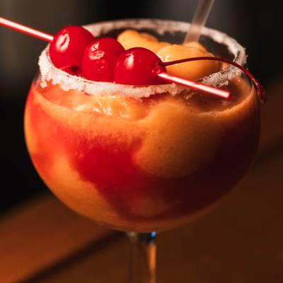 Frozen Margarita cocktail in salt-rimmed glass garnished wirh cherries on the pick.