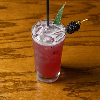 Mora Negra cocktail garnished with a leaf and blackberry.